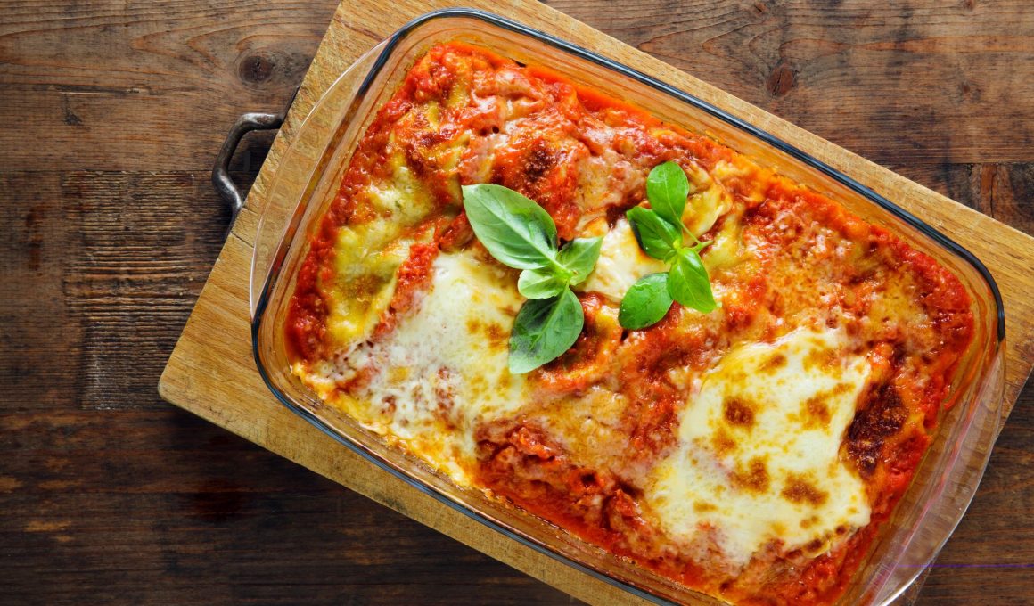 overhead view of a lasagna in a glass dish on a wooden cutting boad