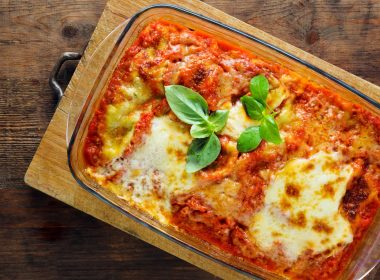 overhead view of a lasagna in a glass dish on a wooden cutting boad